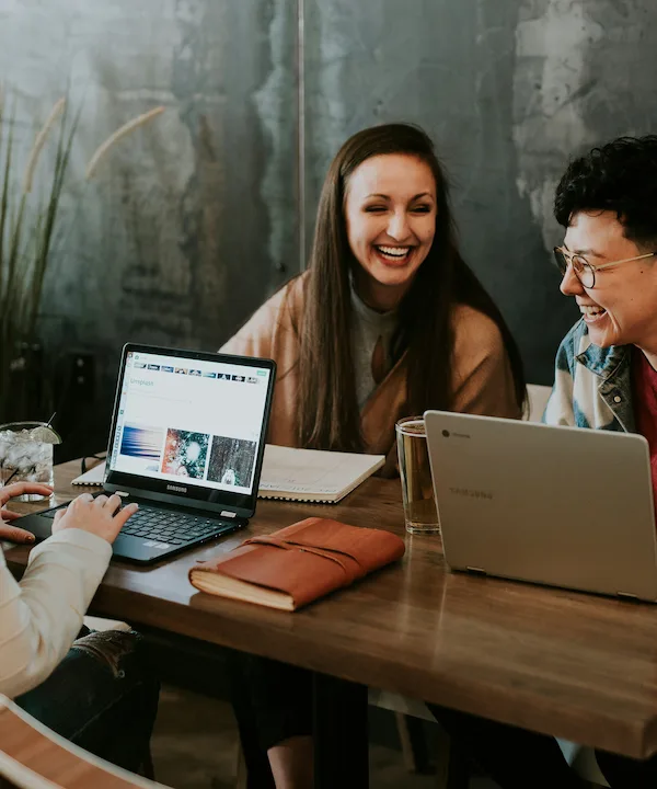 A trio of women working on laptops at a table, immersed in digital marketing tasks and discussions.
